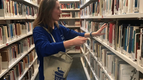 Woman enthusiastically pulling books off the shelf and putting them into her tote bag. 